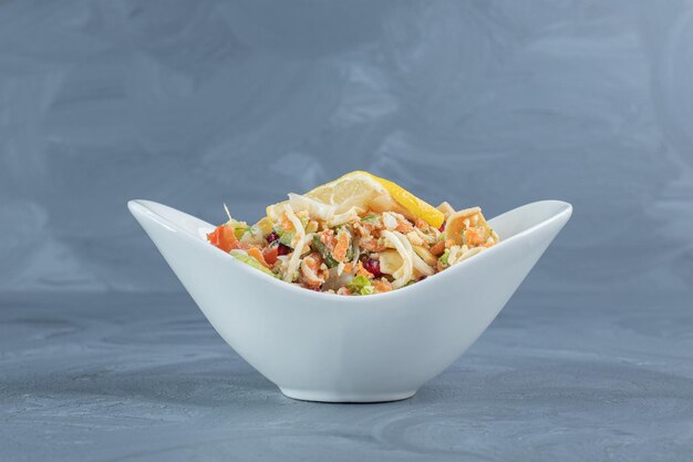 Rodajas de limón colocadas encima de un tazón pequeño de ensalada de verduras mixtas sobre una mesa de mármol.