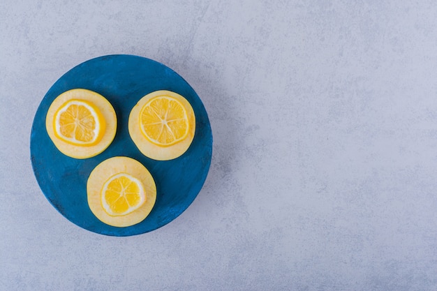 Rodajas de limón y manzana maduras frescas en tablero azul.