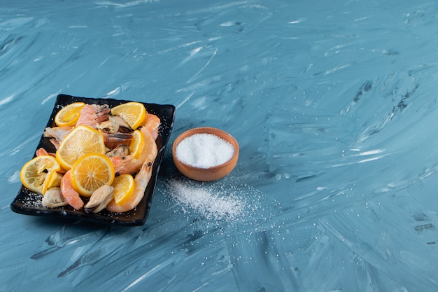 Rodajas de limones y gambas en un plato junto al cuenco de sal, sobre el fondo de mármol.