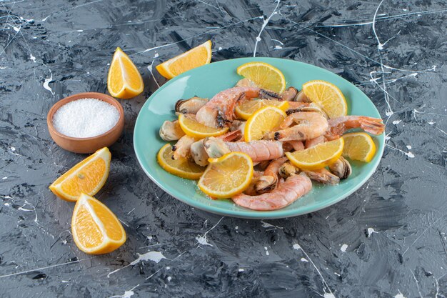 Rodajas de limones y gambas en un plato junto al cuenco de sal, sobre la superficie de mármol.