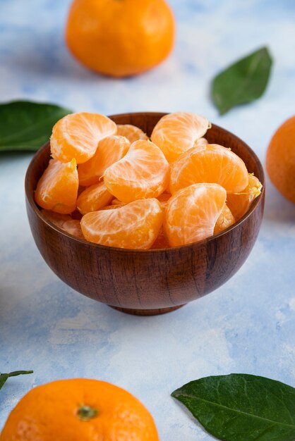 Rodajas de mandarina clementina en un tazón de madera sobre superficie azul