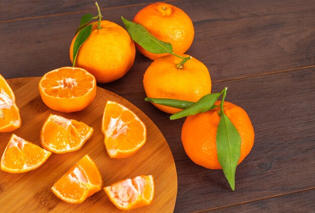 Rodajas de mandarinas en tabla de cortar con mandarinas enteras en mesa de madera