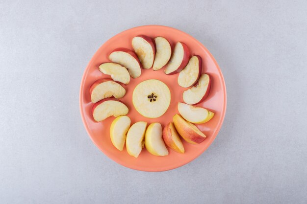 Rodajas de manzanas alrededor de la pera en un plato, sobre el mármol.