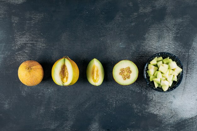 Rodajas de melones con melón en una vista superior de un tazón negro sobre un fondo de madera oscura copia espacio para texto