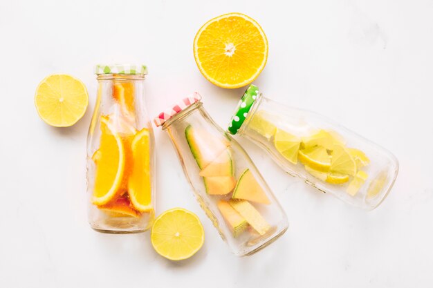 Rodajas de naranja y botellas de vidrio con cítricos cortados.