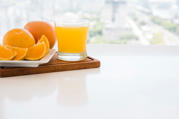 Rodajas de naranja y jugo en la tabla de cortar sobre la mesa blanca