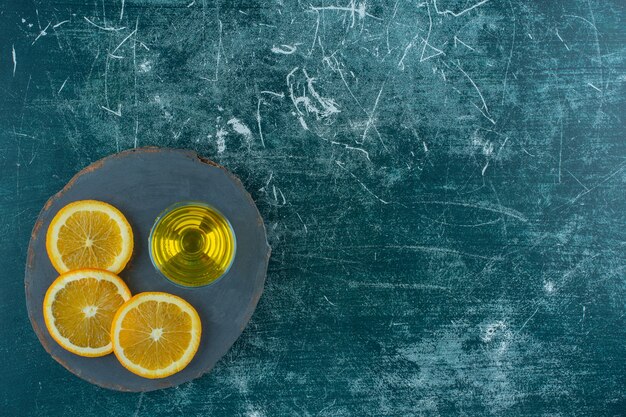 Rodajas de naranja junto al jugo de pera en el tablero, en la mesa azul.