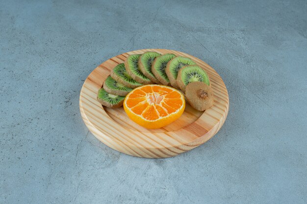 Rodajas de naranja y kiwi en una placa de madera, sobre el fondo de mármol.