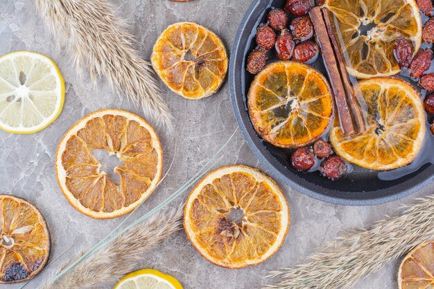 Rodajas de naranja y limón secas con canela sobre la superficie de la piedra.