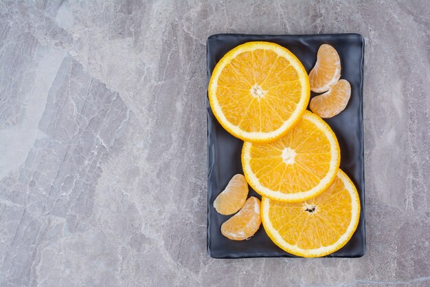 Rodajas de naranja y mandarina en placa negra.