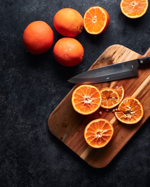 Rodajas de naranjas y un cuchillo sobre una tabla de cortar sobre una mesa negra