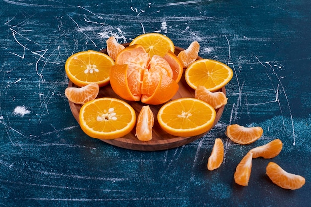 Rodajas de naranjas y mandarinas aisladas en un plato de madera sobre fondo azul. Foto de alta calidad