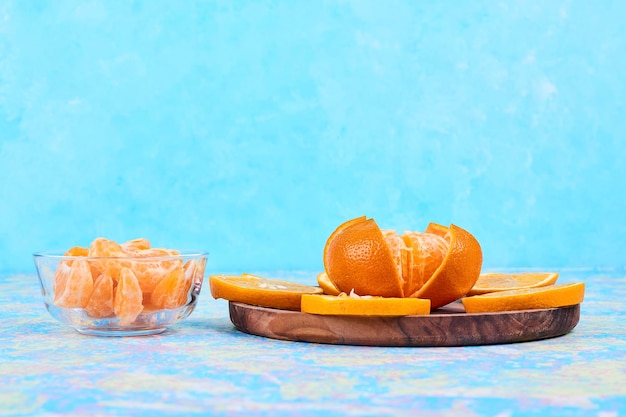 Rodajas de naranjas y mandarinas aisladas en un plato de madera y en un vaso sobre fondo azul. Foto de alta calidad