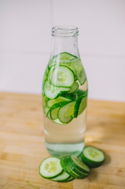 Rodajas de pepino en la botella de agua de vidrio en el escritorio de madera