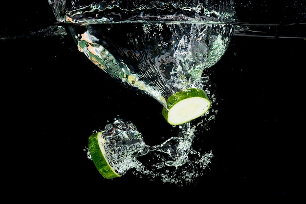 Rodajas de pepino chapoteando en el agua sobre el fondo negro