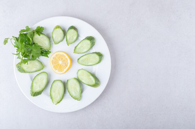 Rodajas de pepino, limón y perejil en un plato, sobre el mármol.