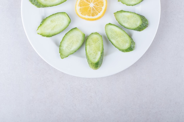 Foto gratuita rodajas de pepino, limón y perejil en un plato, sobre el mármol.