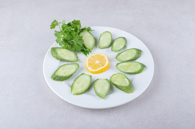 Rodajas de pepino, limón y perejil en un plato, sobre el mármol.