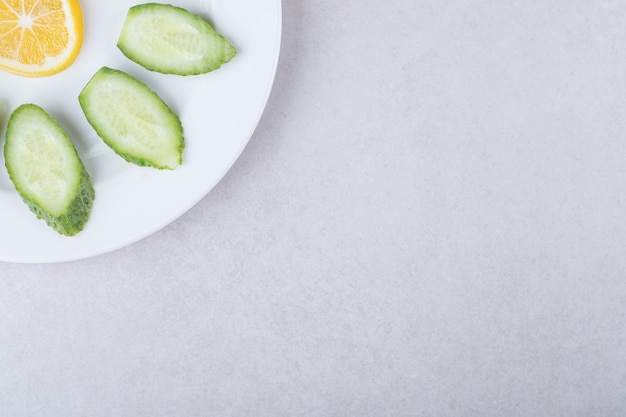 Rodajas de pepino, limón y perejil en un plato sobre la mesa de mármol.