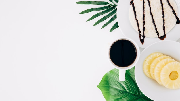 Foto gratuita rodajas de piña; tortillas y café beben en hojas verdes sobre fondo blanco