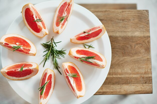 Rodajas de pomelo fresco y romero en plato blanco. Desde arriba. Comida saludable dieta saludable