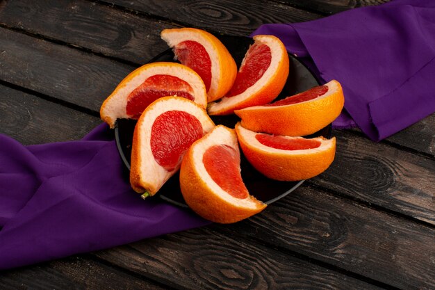 Rodajas de pomelo naranja jugoso dentro de un plato negro sobre un pañuelo morado y un escritorio de madera marrón