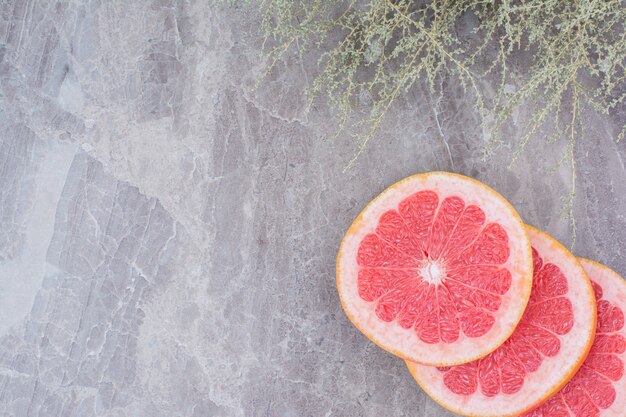 Rodajas de pomelo sobre fondo de piedra con planta.