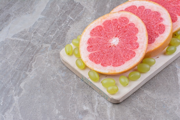 Rodajas de pomelo y uvas sobre tabla de madera.