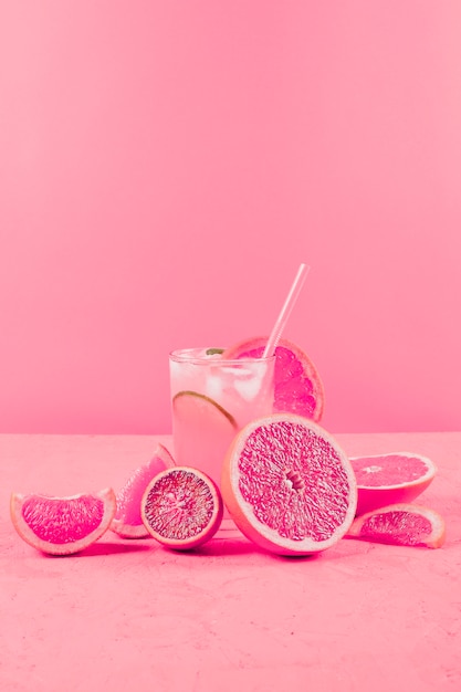 Rodajas de pomelo y vaso de jugo sobre fondo rosa con textura