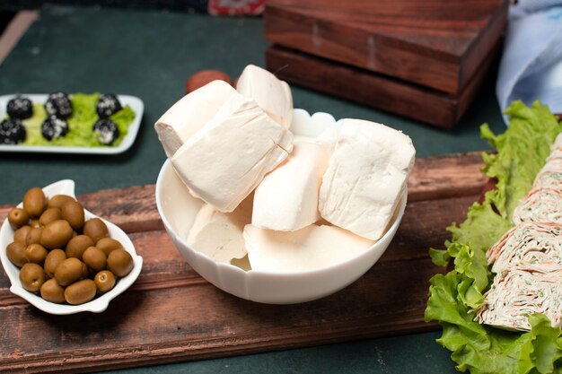 Rodajas de queso blanco en un bol con aceitunas verdes