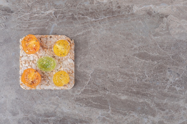 Rodajas de tomate condimentado con torta de arroz debajo, sobre la superficie de mármol