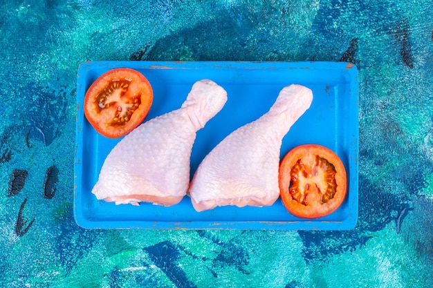Rodajas de tomate y muslo de pollo crudo sobre una placa de madera