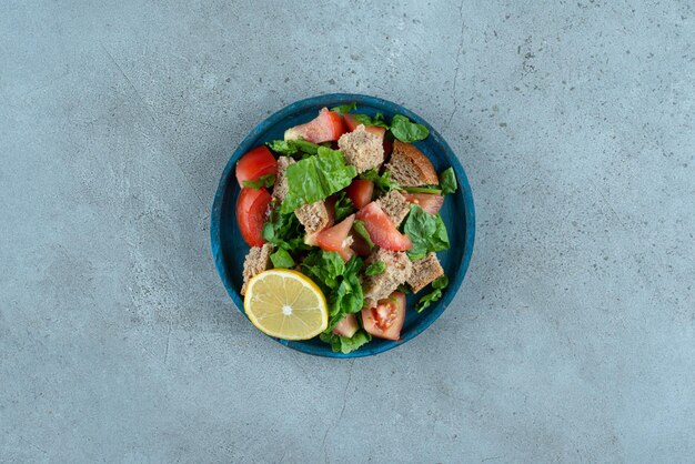 Rodajas de tomate, pan, limón y verduras en placa azul.