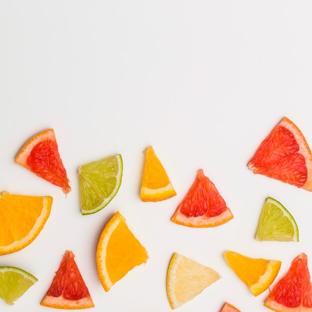 Rodajas triangulares de naranjas; pomelo y limón sobre fondo blanco