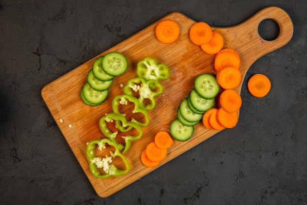Foto gratuita rodajas de zanahoria y pepino y pimiento sobre tabla de cortar de madera sobre negro