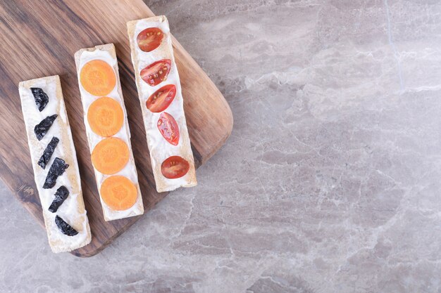 Rodajas de zanahorias, ciruelas y tomates sobre panes crujientes, sobre la superficie de mármol