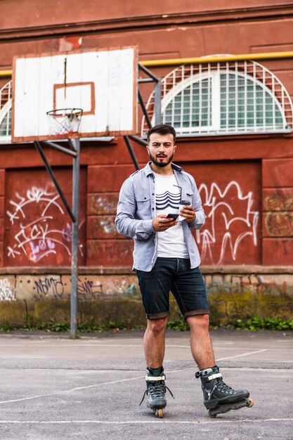 Rollerskater masculino que usa el teléfono móvil en la cancha de básquet