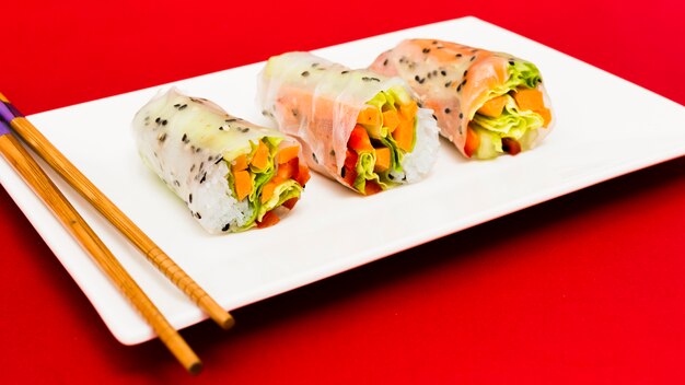 Rollitos de primavera al vapor organizan en un plato blanco con palillos sobre una superficie roja