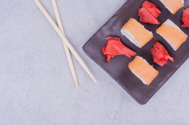 Rollitos de salmón y jengibre rojo marinado en bandeja negra.