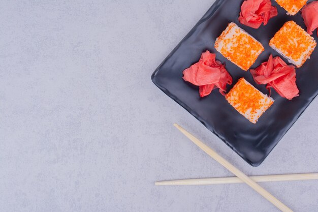 Rollitos de salmón y jengibre rojo marinado en bandeja negra.