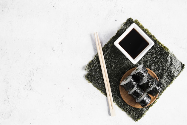 Rollitos de sushi con salsa de soja y palillos sobre algas.