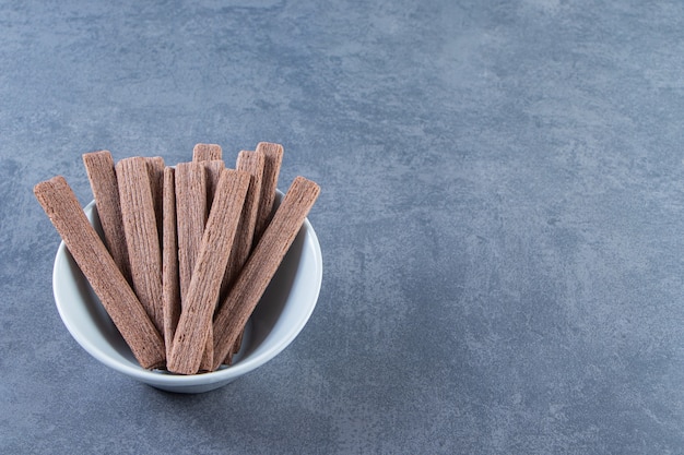 Rollo de obleas de chocolate delicioso en un recipiente sobre la superficie de mármol