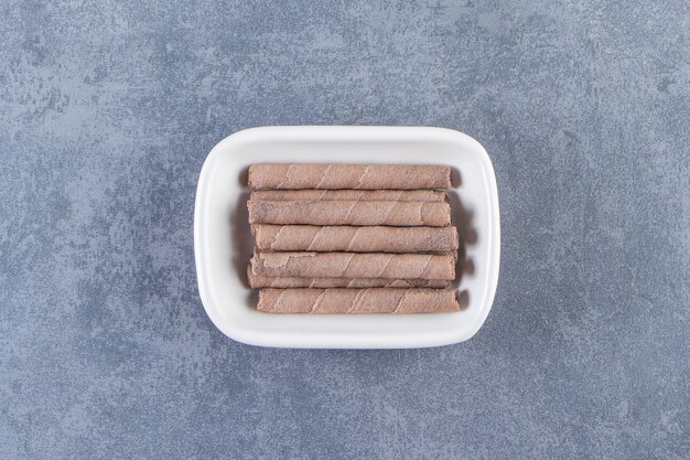 Rollo de obleas de chocolate con dientes en un cuenco, sobre el fondo de mármol.