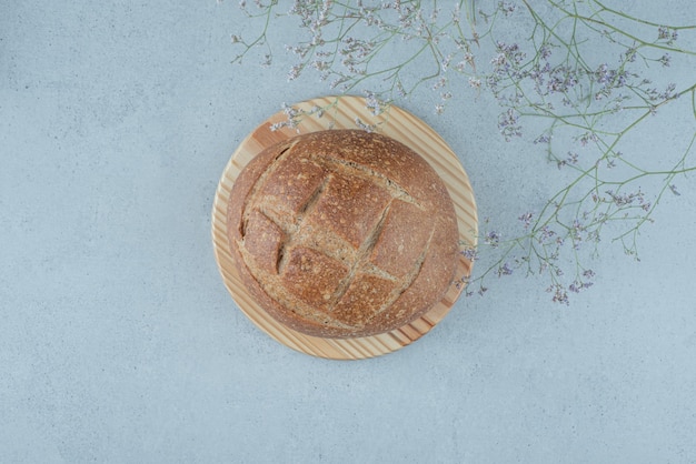 Rollo de pan de centeno sobre tabla de madera con planta