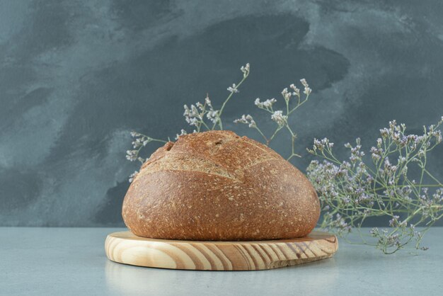 Rollo de pan de centeno sobre tabla de madera con planta