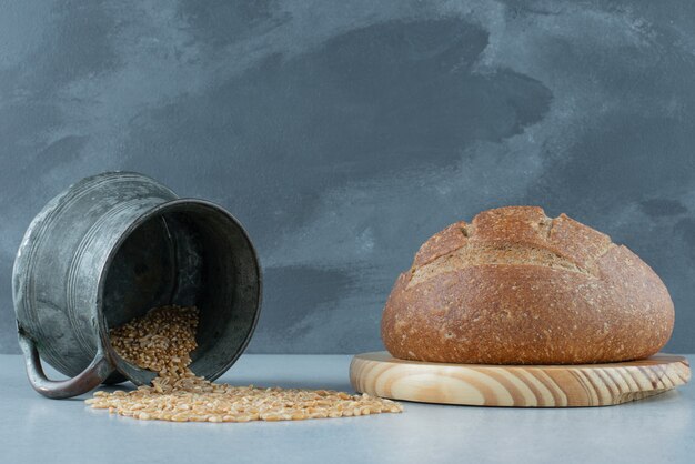 Rollo de pan de centeno sobre tabla de madera con taza de cebada