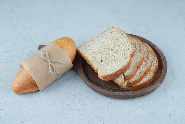 Rollo de pan y rebanadas de pan en placa de madera