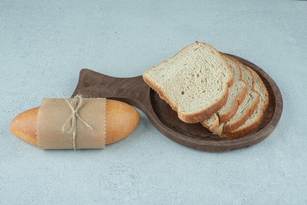 Rollo de pan y rebanadas de pan en placa de madera