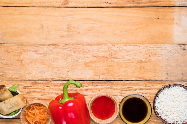 Rollo de primavera; pimiento rojo; Salsas y tazón de arroz en mesa de madera