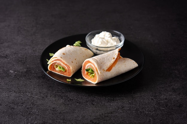 Rollo de sándwich de envoltura de salmón con queso y verduras sobre fondo de piedra negra